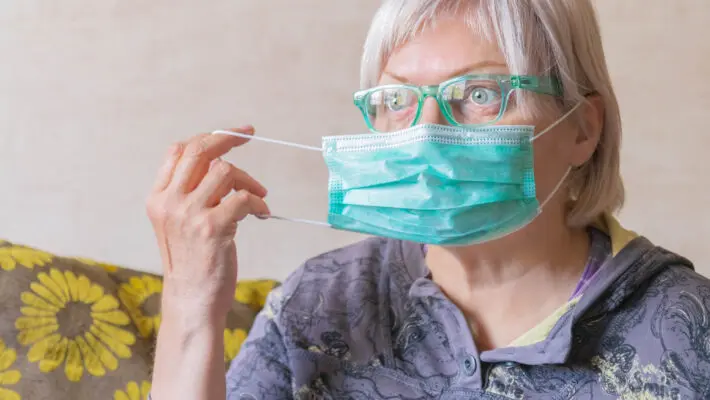Elderly woman putting on medical protective face mask before going outside