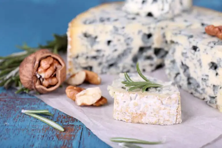 Blue cheese with sprigs of rosemary and nuts on sheet of paper and color wooden table background