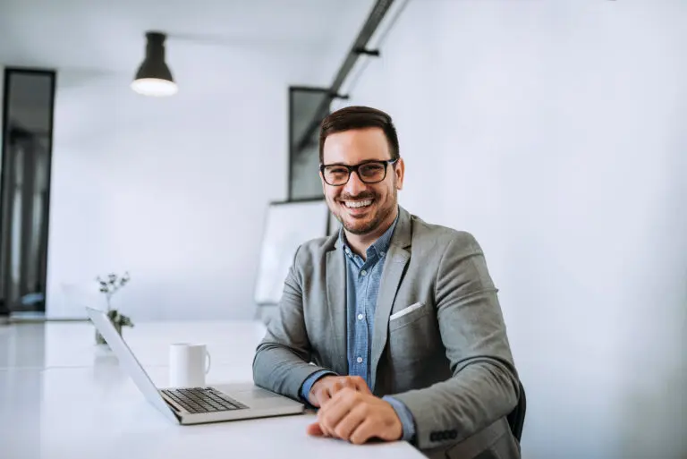 Young,Smiling,Entrepreneur,In,Bright,Office,Working,On,Laptop.