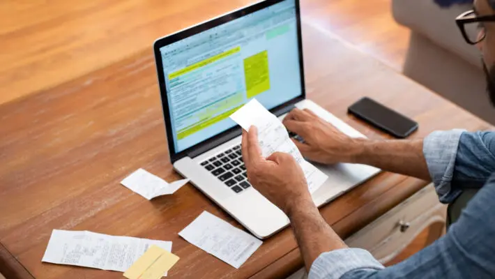 Hands,Of,Businessman,Analyzing,Invoice,On,Laptop,While,Checking,Bills.