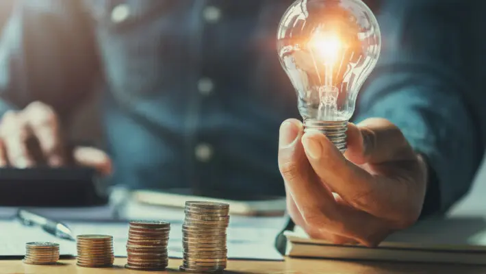 Business,Man,Hand,Holding,Lightbulb,With,Using,Calculator,To,Calculate