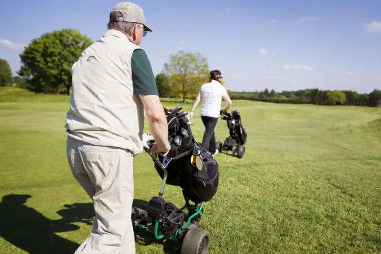 Active,Senior,Golf,Couple,Pushing,Golf,Trolley,With,Bag,On