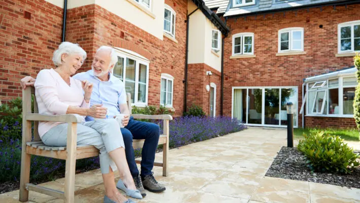 Retired,Couple,Sitting,On,Bench,With,Hot,Drink,In,Assisted