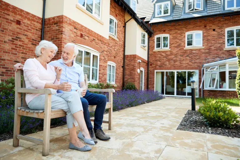 Retired,Couple,Sitting,On,Bench,With,Hot,Drink,In,Assisted