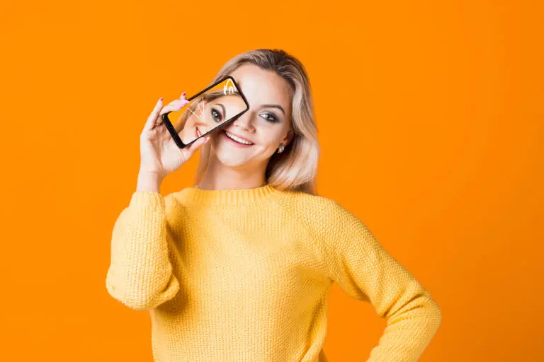 Cute,Young,Woman,In,A,Yellow,Sweater,Holding,A,Smartphone