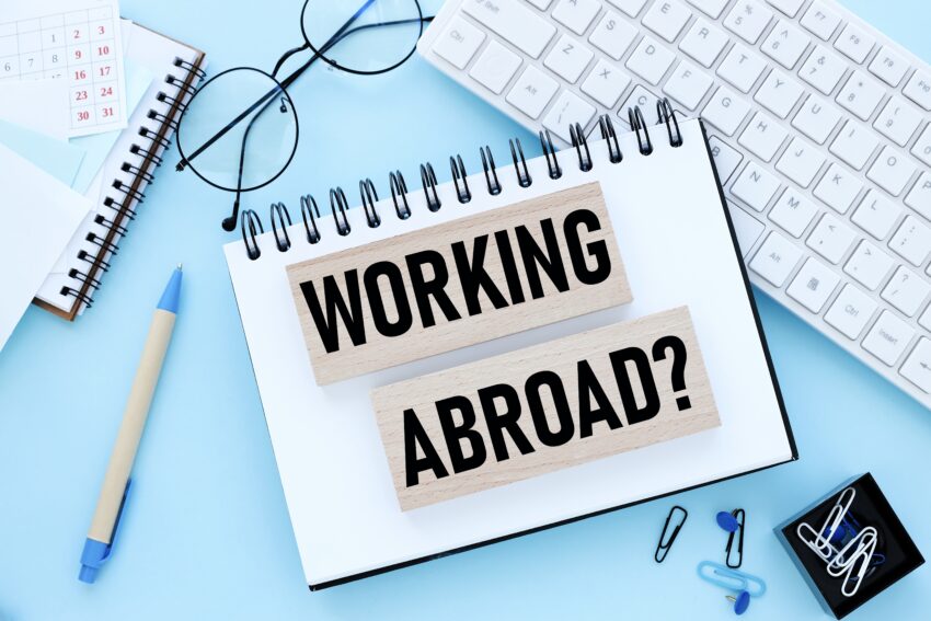 Working,Abroad.,Text,On,Wooden,Blocks,On,A,Blue,Background.