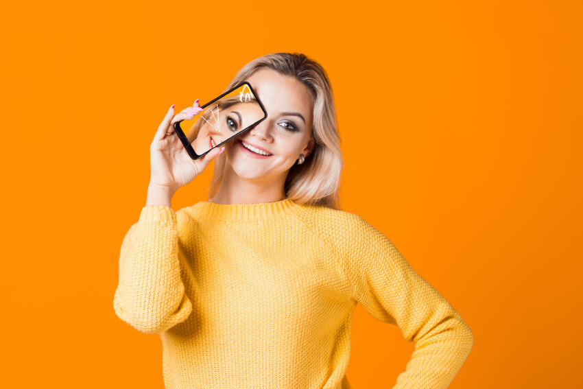 Cute,Young,Woman,In,A,Yellow,Sweater,Holding,A,Smartphone